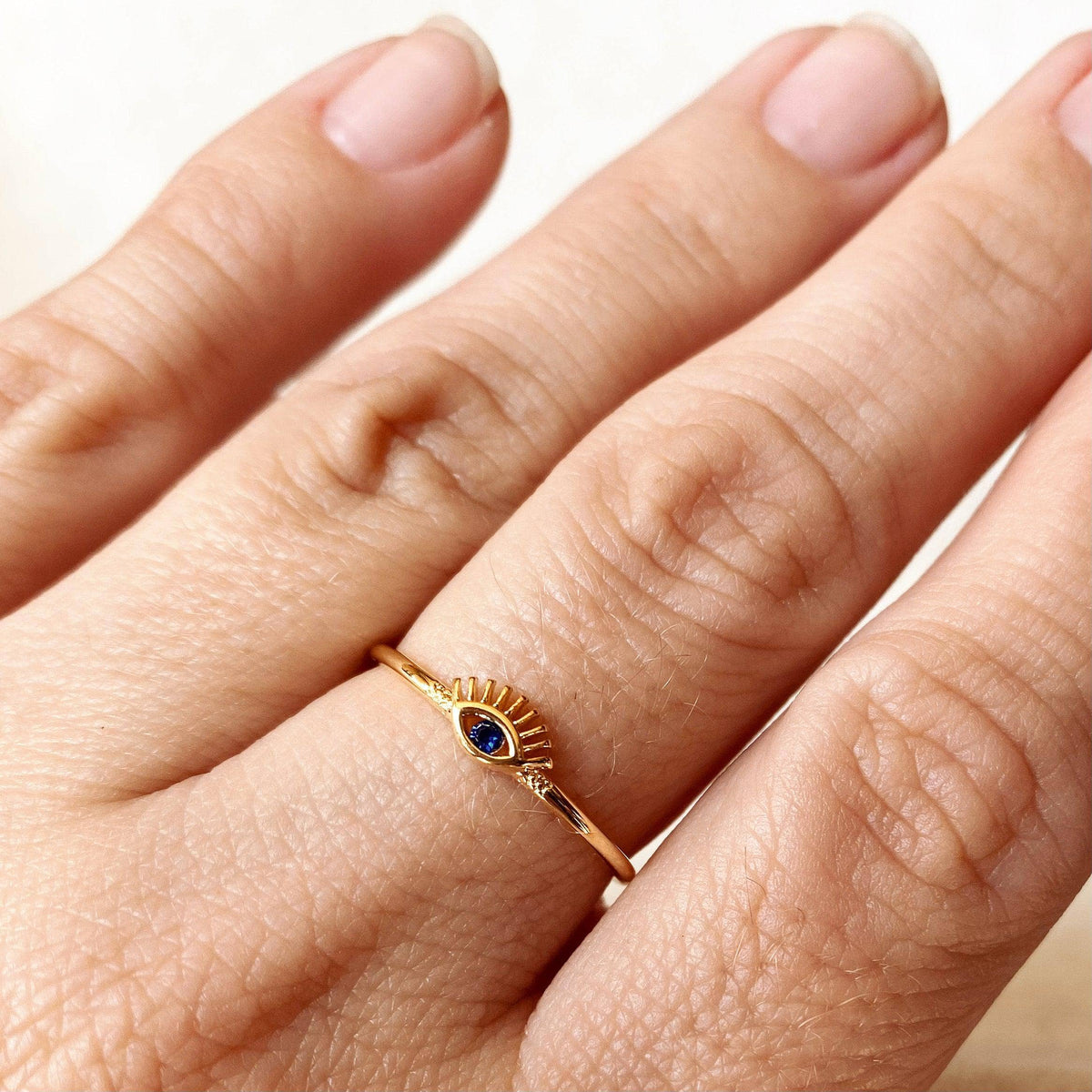 Gold ring with a blue gemstone on a person's finger against a neutral background