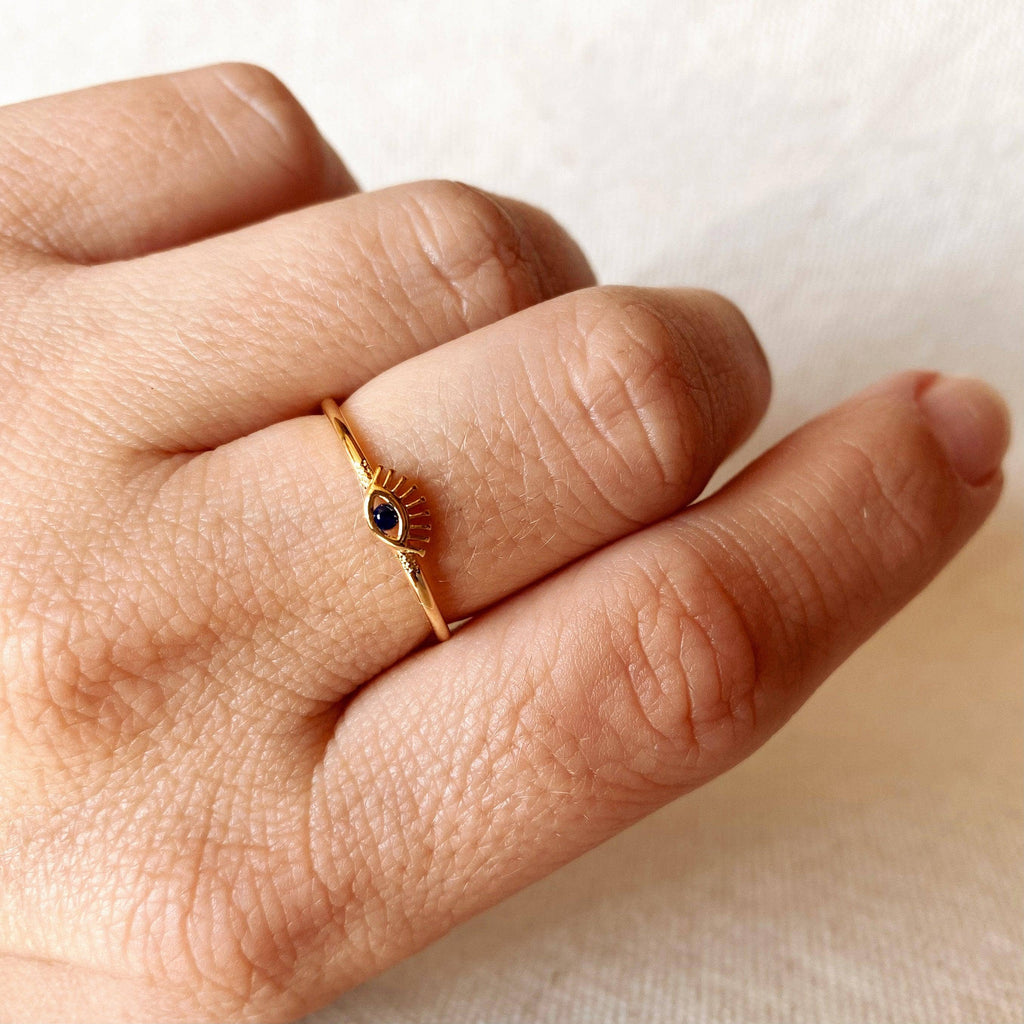 Gold ring with a black gemstone on a person's finger against a neutral background