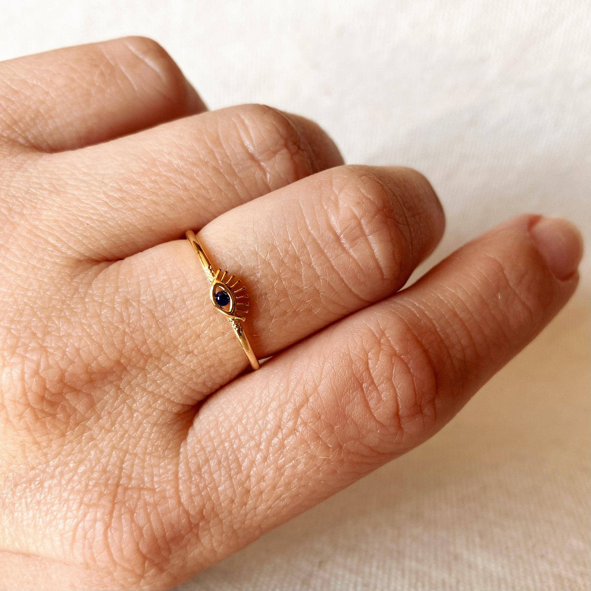 Gold ring with a black gemstone on a person's finger against a neutral background