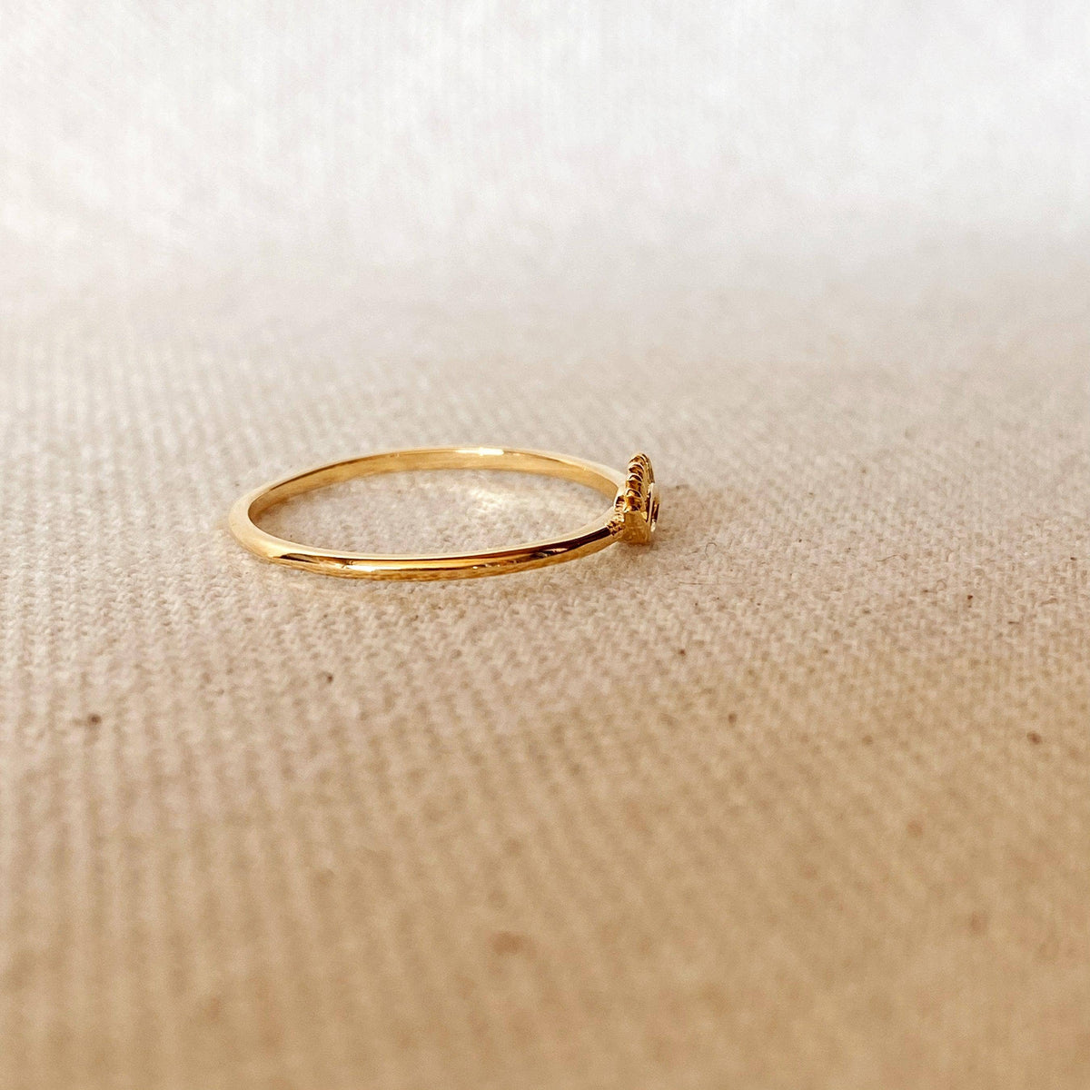 Gold ring with a small decorative element on a beige fabric background