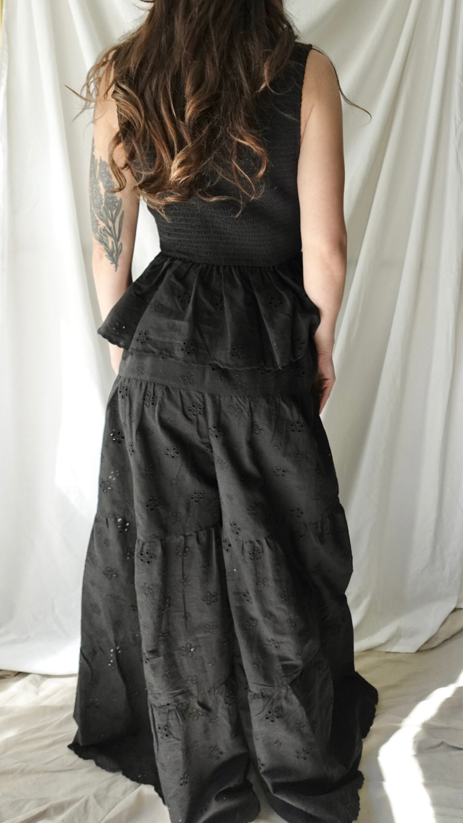 Black sleeveless dress with peplum waist against a white curtain background