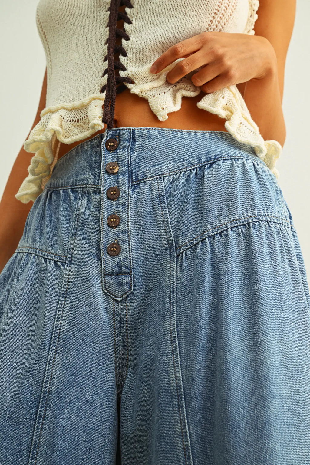 Person wearing a beige lace top and blue denim pants with button details.