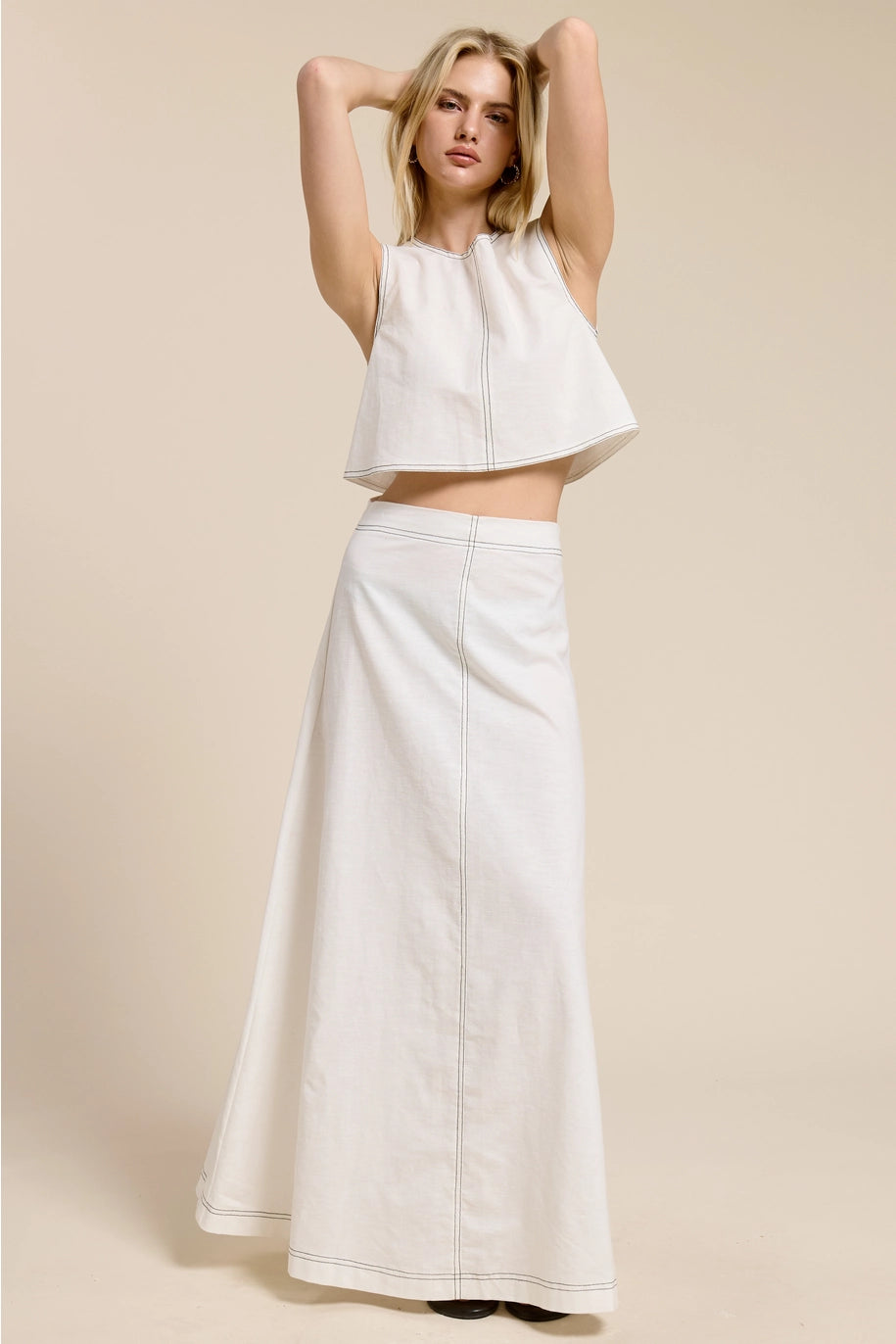 Woman wearing a white sleeveless top and long skirt against a beige background
