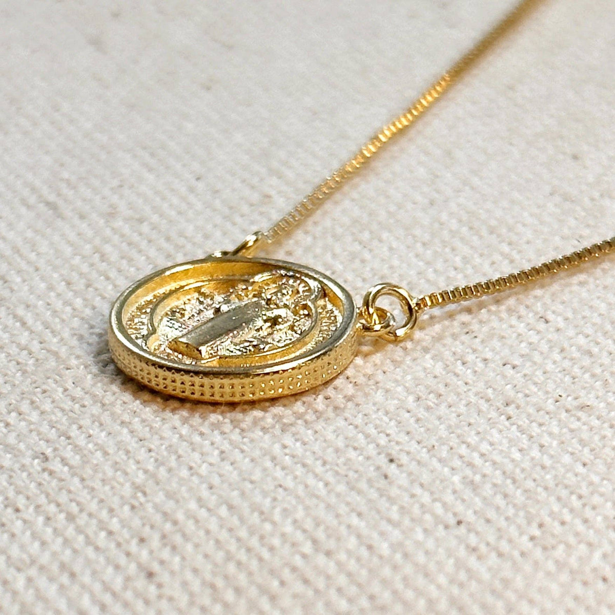 Gold necklace with a round pendant on a textured beige background