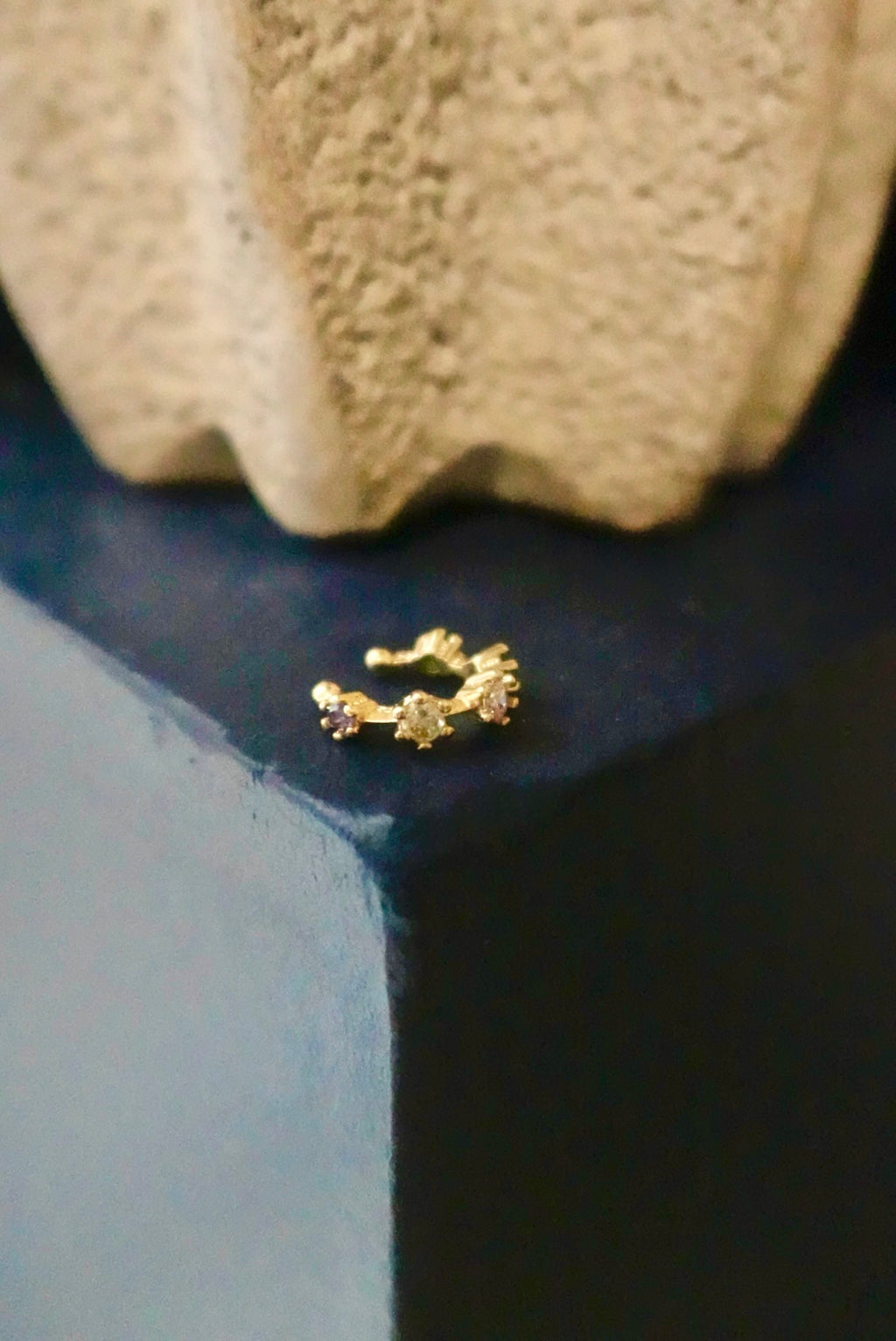 Gold earring on a dark surface with a textured beige object in the background