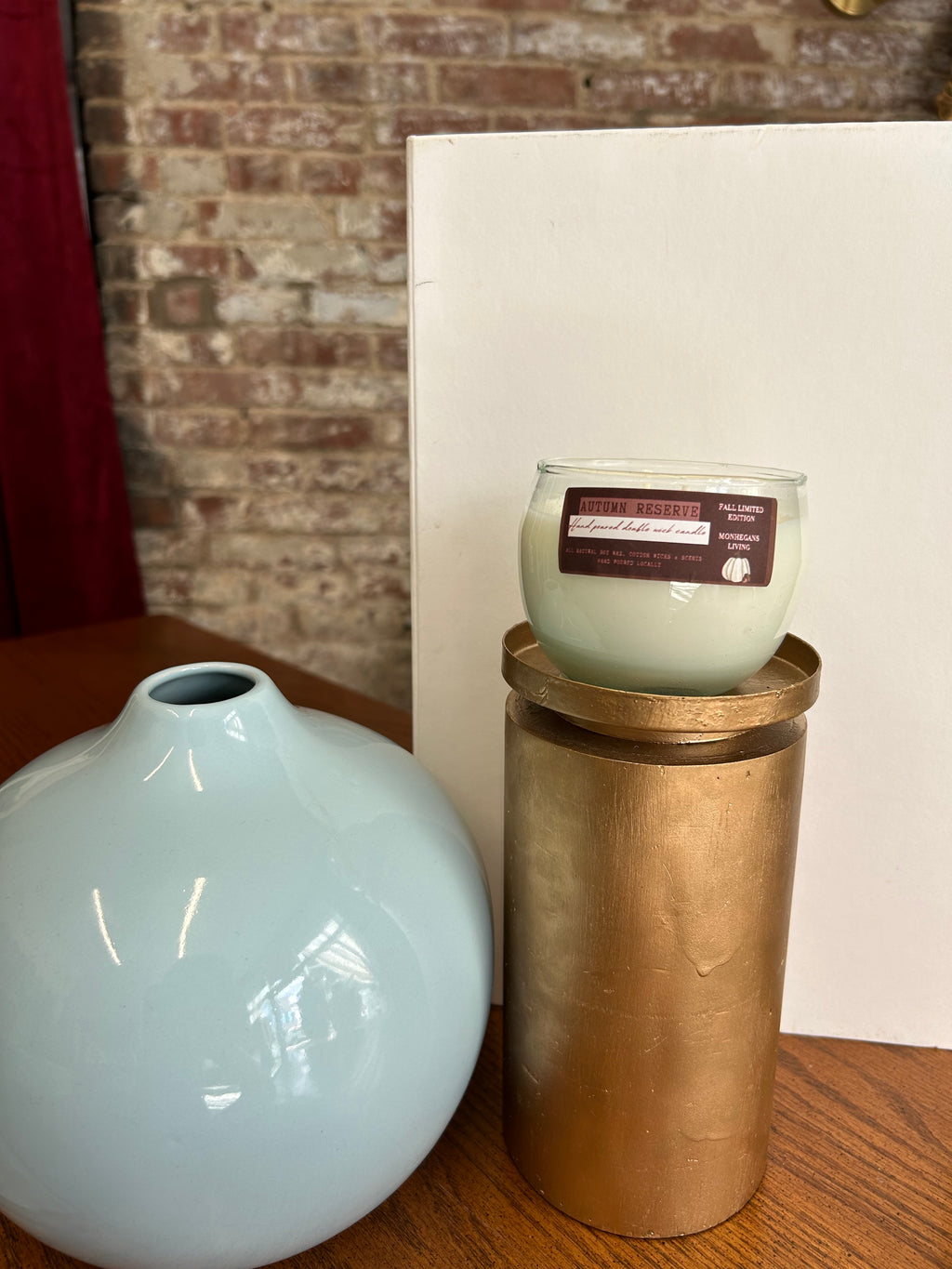 Decorative objects including a cylindrical brass item, glass container, and white vase on a textured surface.