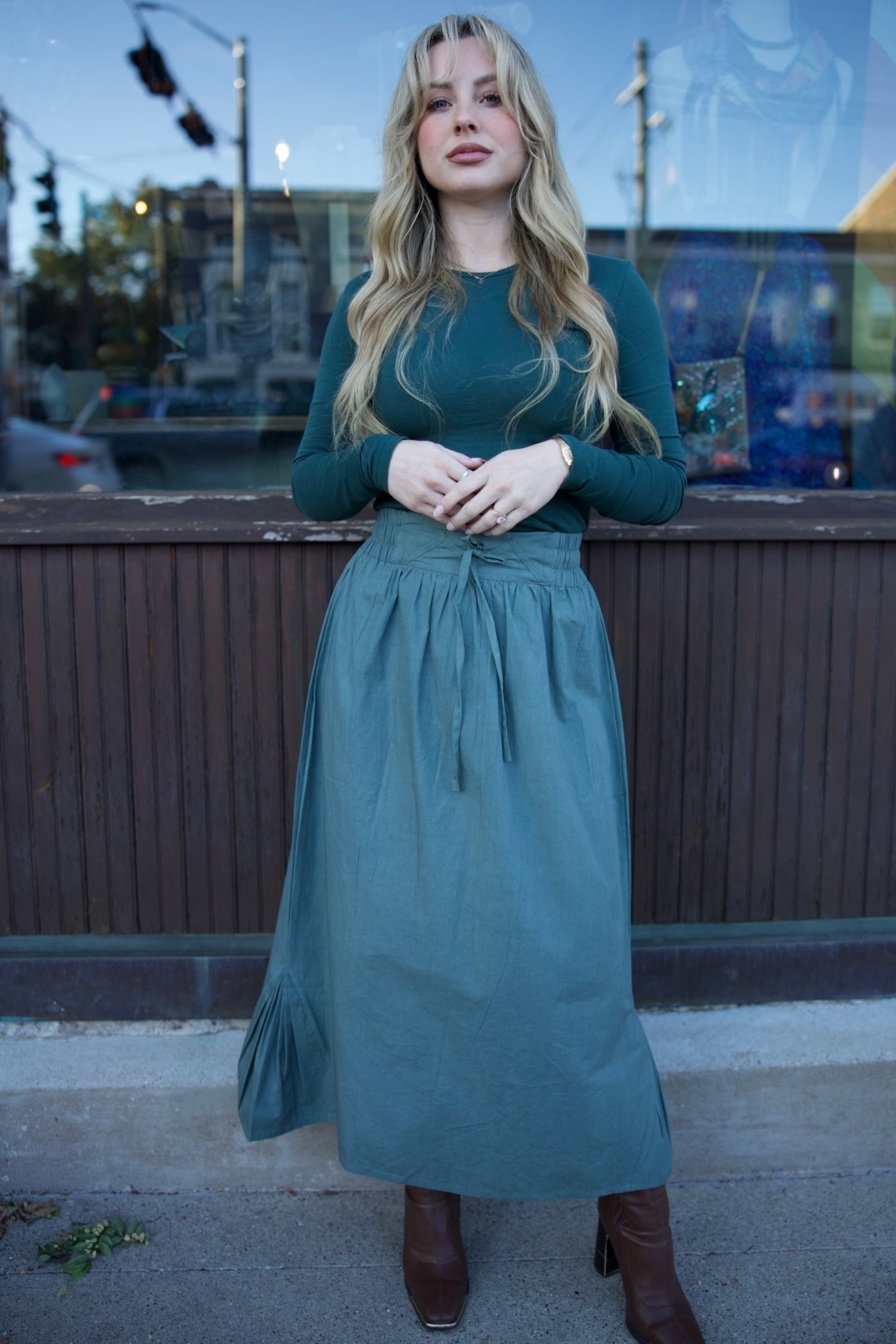 Woman in a teal dress standing on a sidewalk with a cityscape background