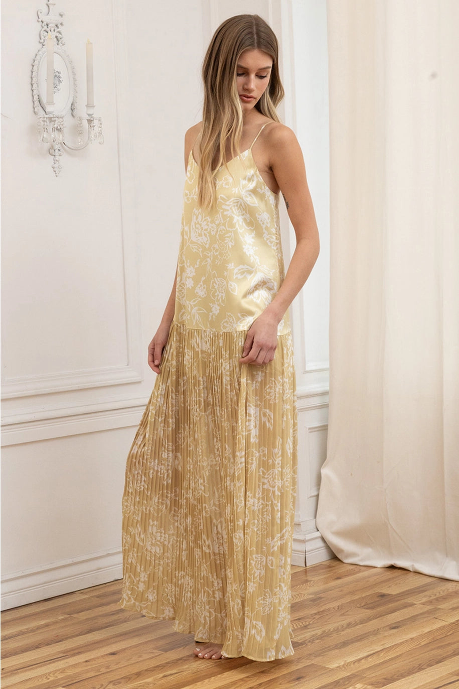 Woman wearing a gold floral dress standing in a room with white walls and wooden floor.