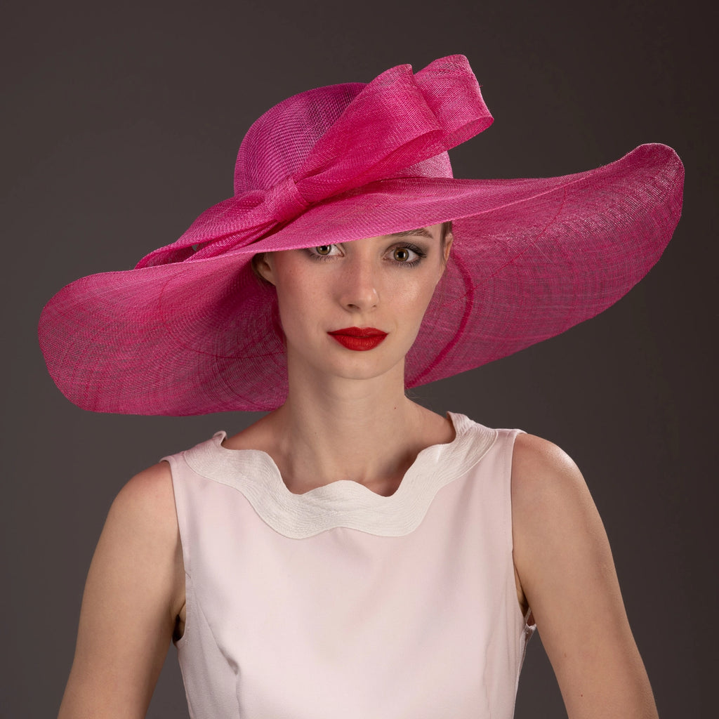 Woman wearing a large pink hat against a dark background