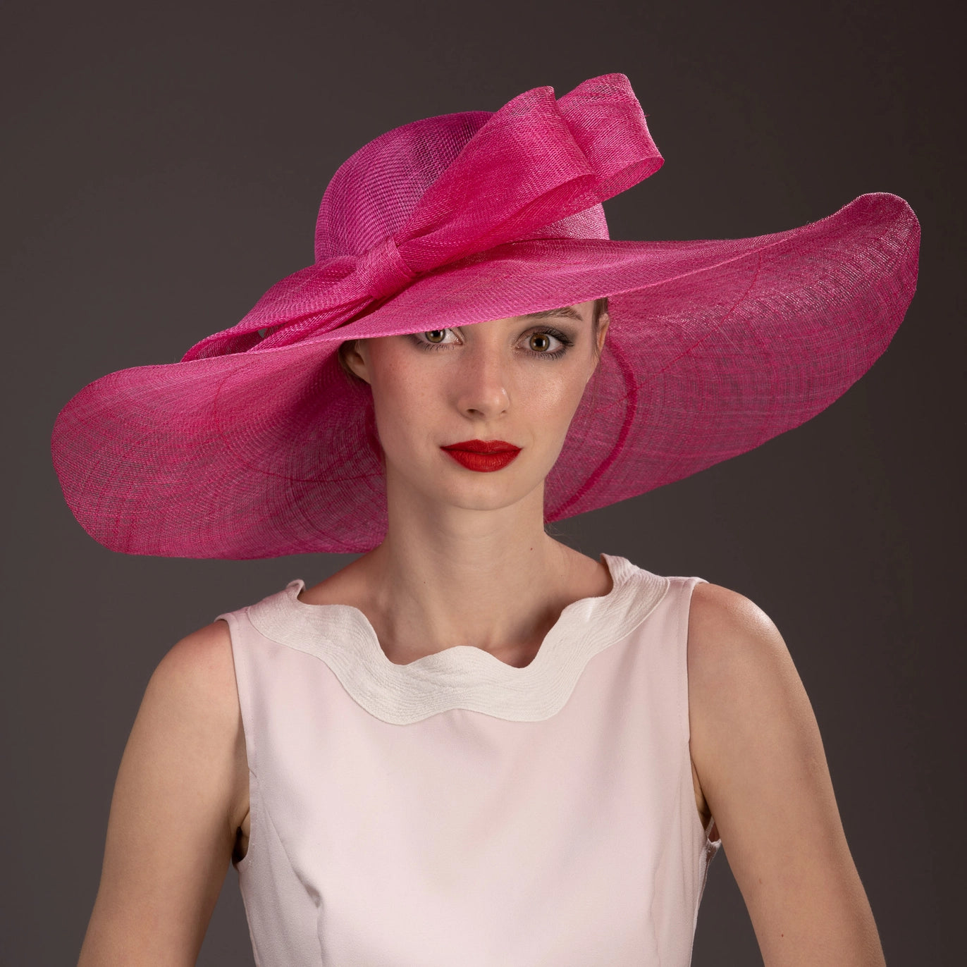 Woman wearing a large pink hat against a dark background