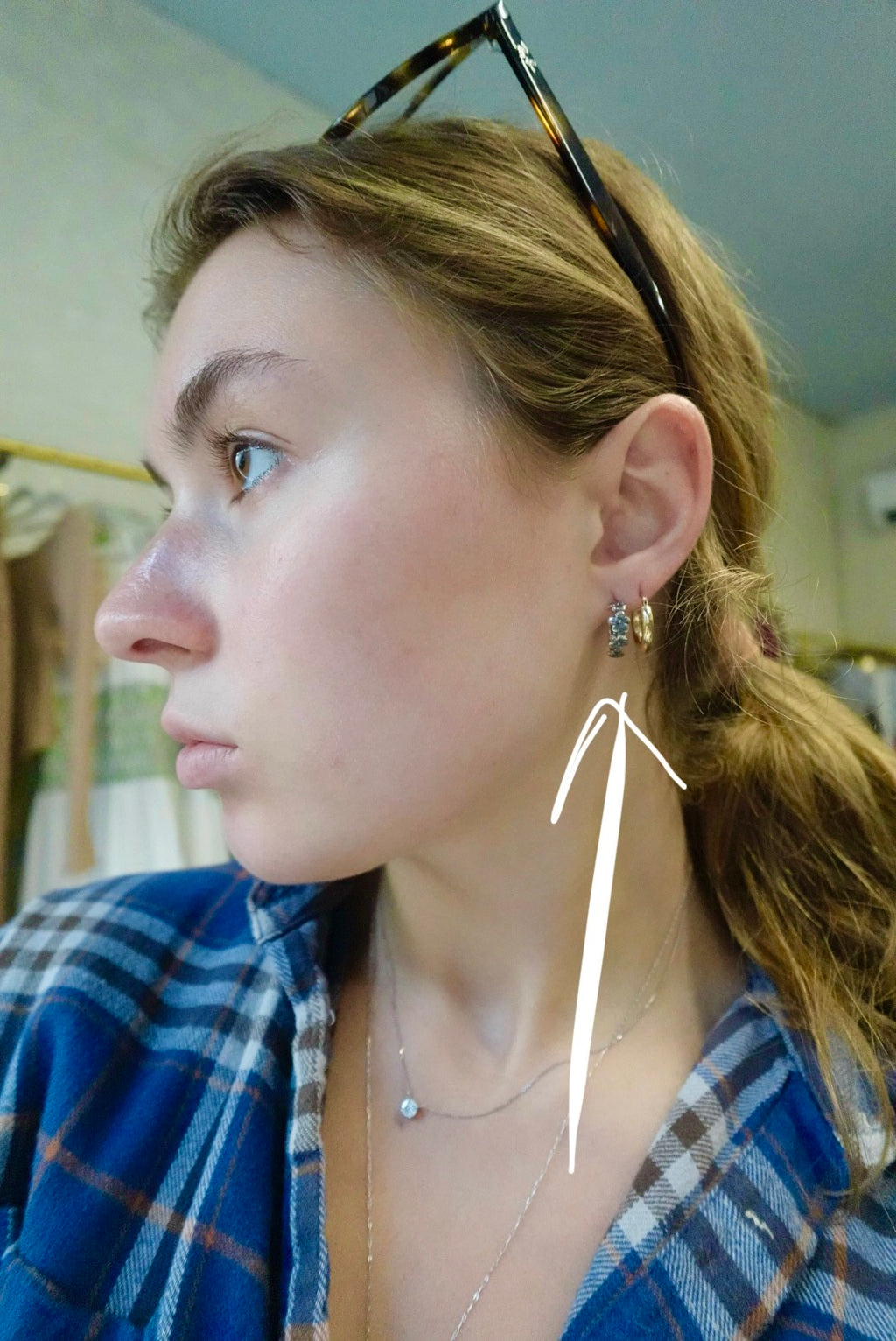 Person wearing a blue plaid shirt with a necklace, earrings, and sunglasses on their head.