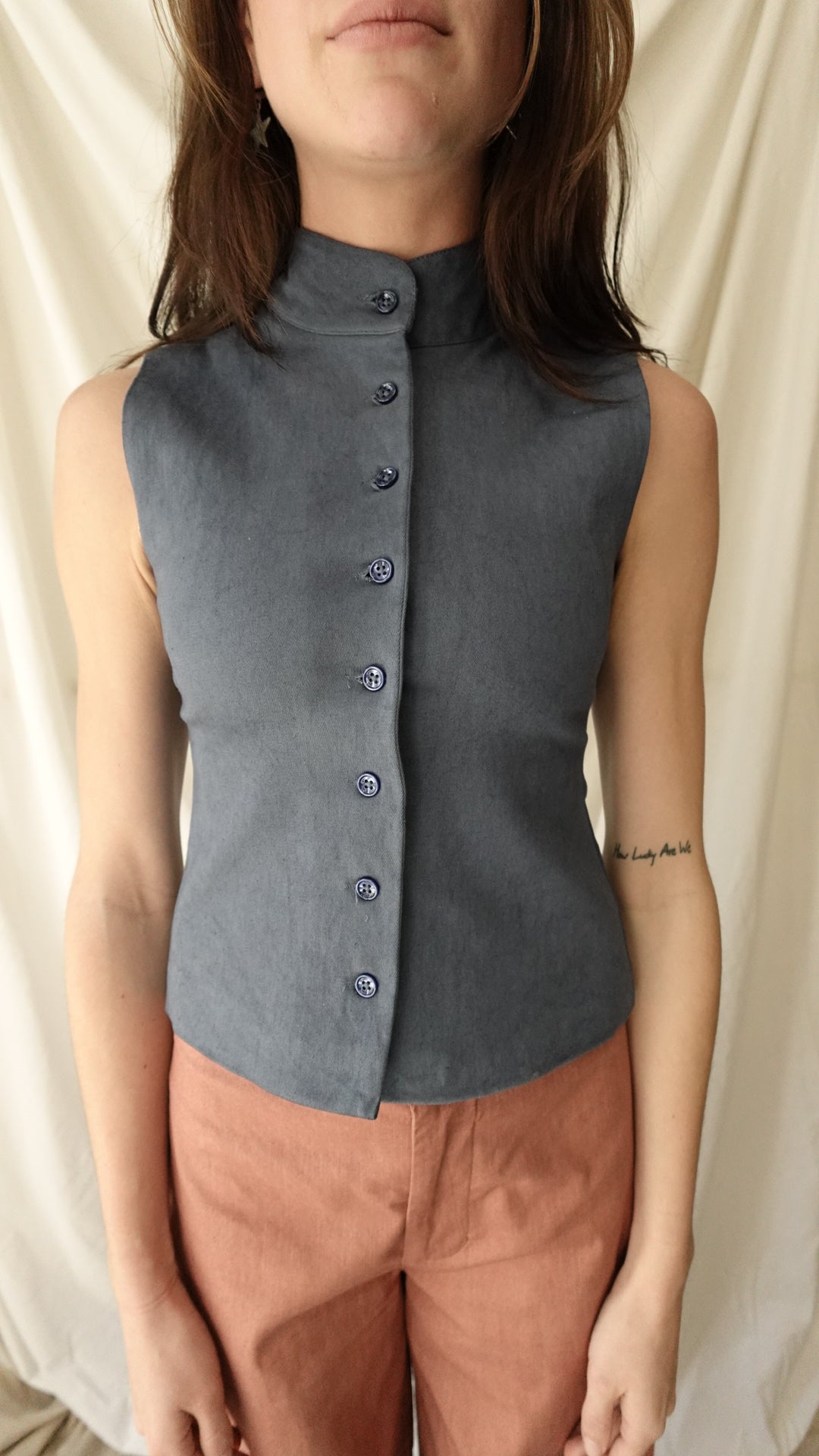 Woman wearing a sleeveless dress with button details on a beige background