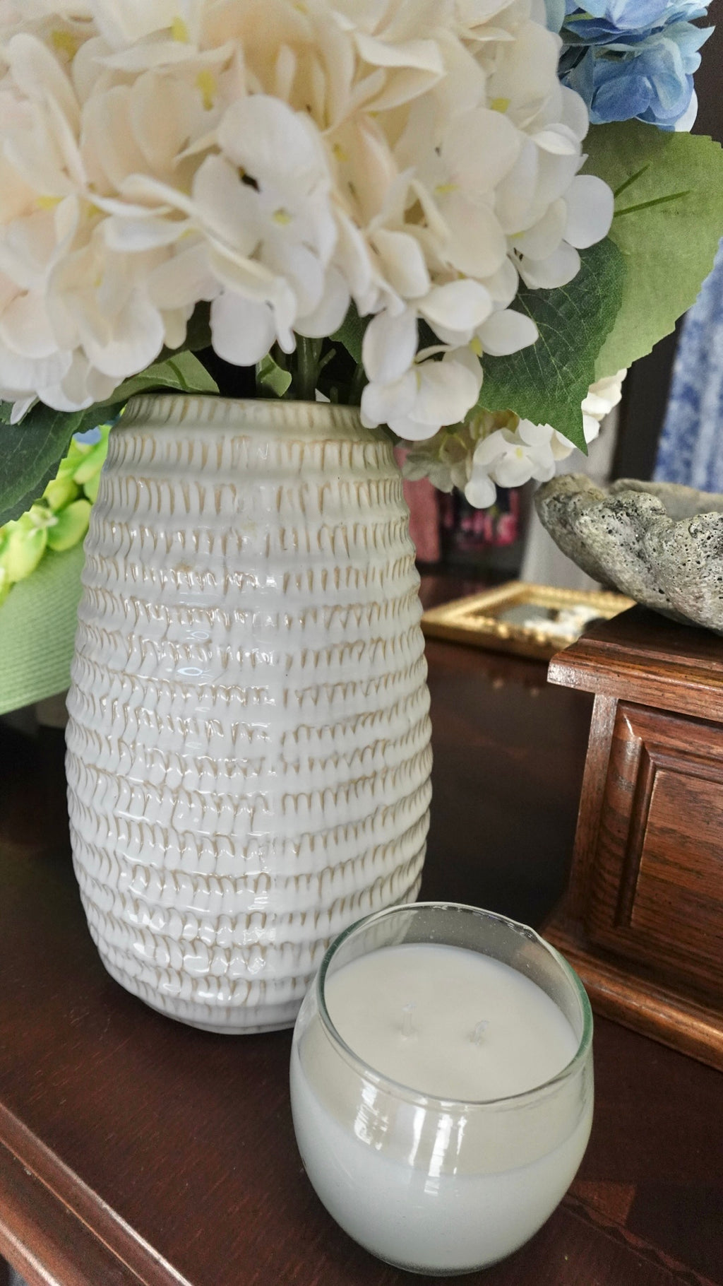 White textured vase with flowers and a glass of milk on a wooden surface