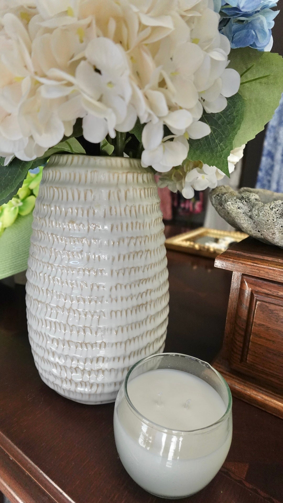 White textured vase with flowers and a glass of milk on a wooden surface