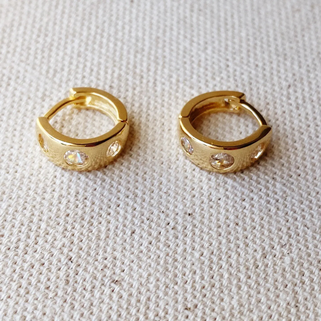 Gold hoop earrings with embedded stones on a textured beige surface