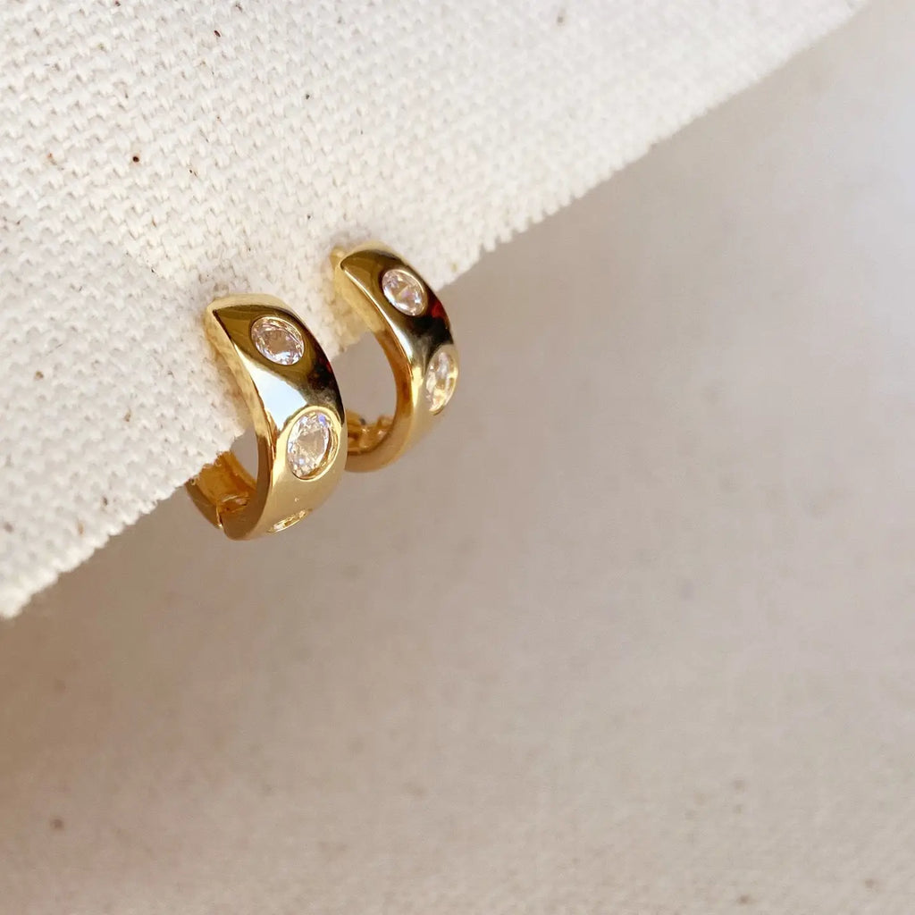Gold hoop earrings with embedded stones on a textured beige surface