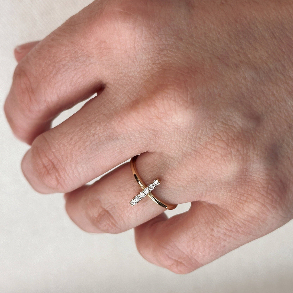 Hand wearing a gold ring with a diamond on a neutral background