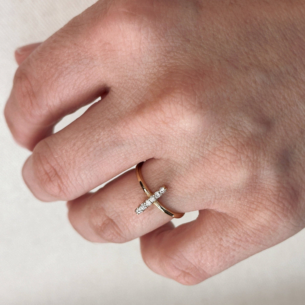 Hand wearing a gold ring with a diamond on a neutral background