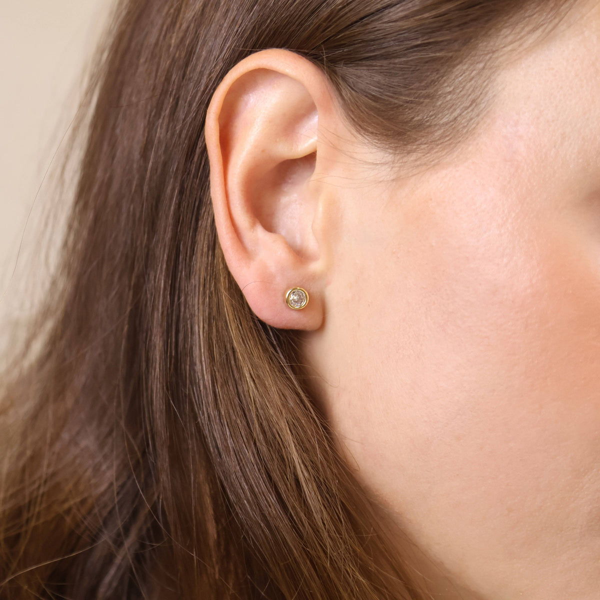 Close-up of an ear wearing a gold earring with a neutral background