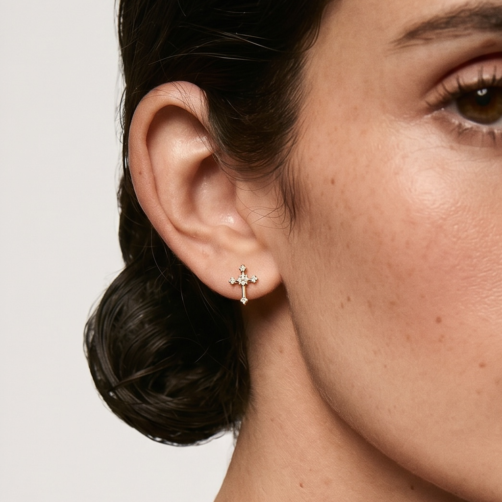 Close-up of a woman wearing a gold cross earring on a plain background