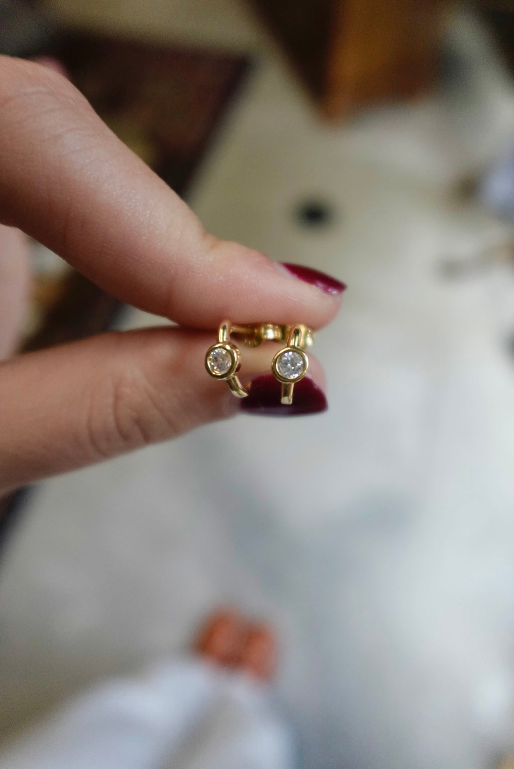 Gold hoop earrings with gemstones held between fingers against a blurred background