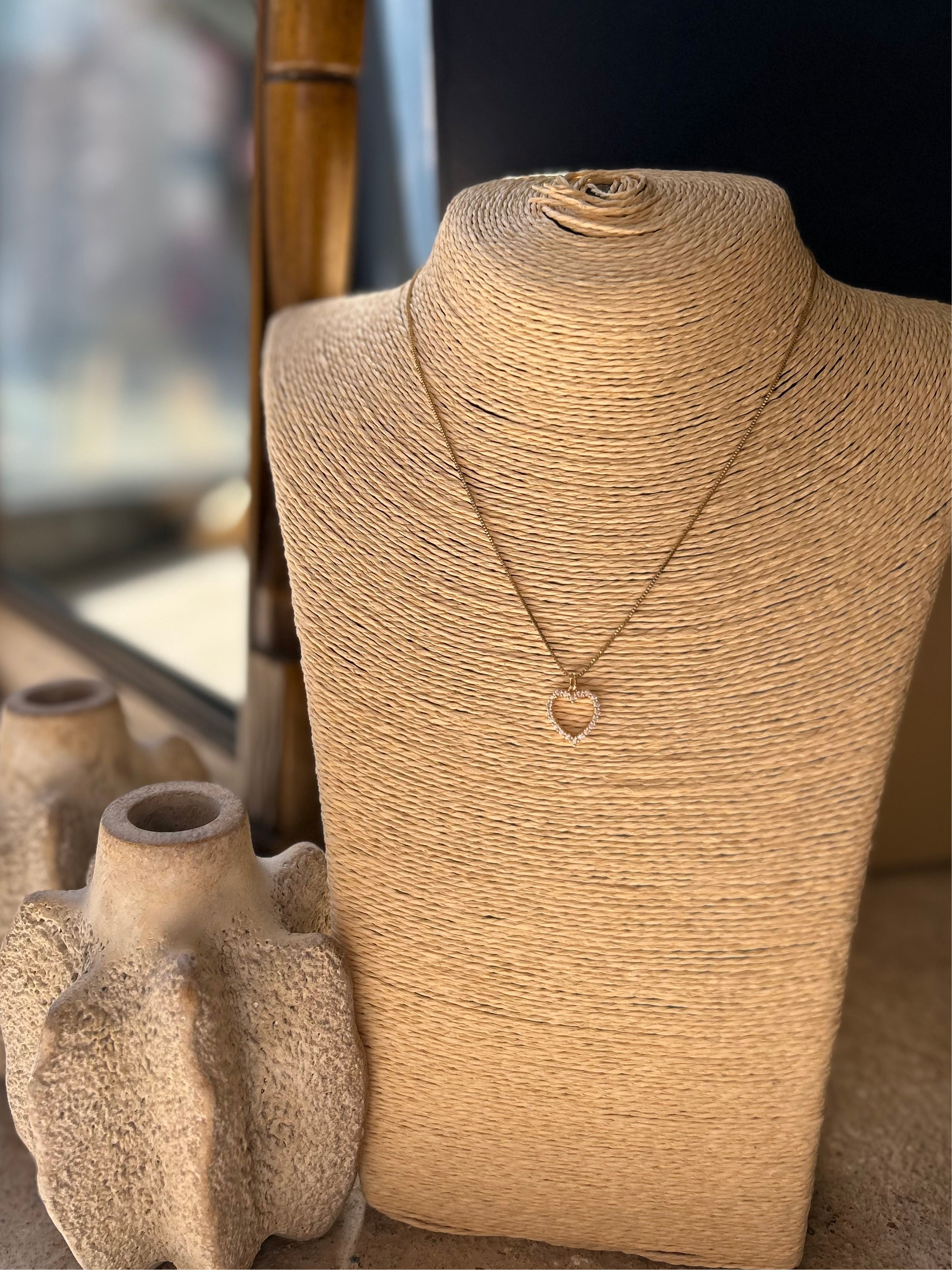 Necklace with a heart pendant on a textured mannequin bust next to ceramic vases.