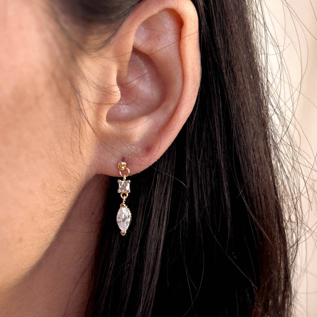Close-up of an ear wearing a gold earring with clear stones.