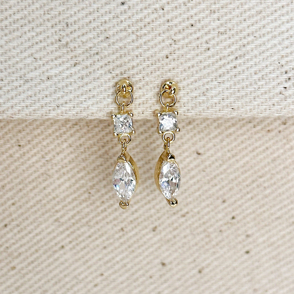Gold earrings with clear gemstones on a textured beige background