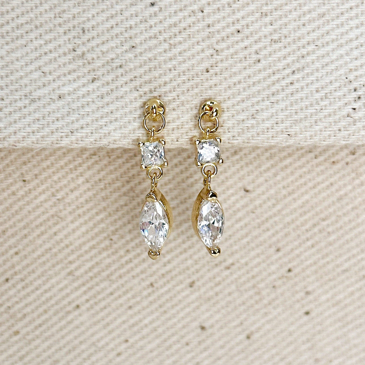 Gold earrings with clear gemstones on a textured beige background