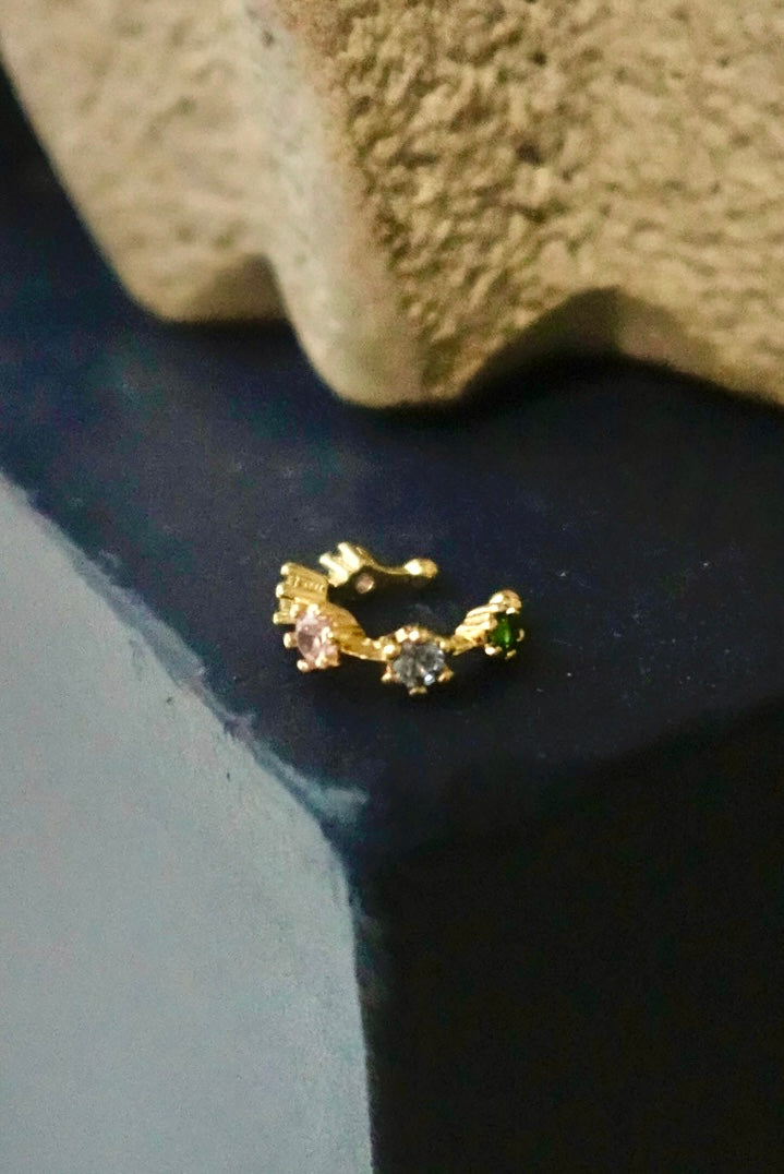 Gold earring with gemstones on a textured surface