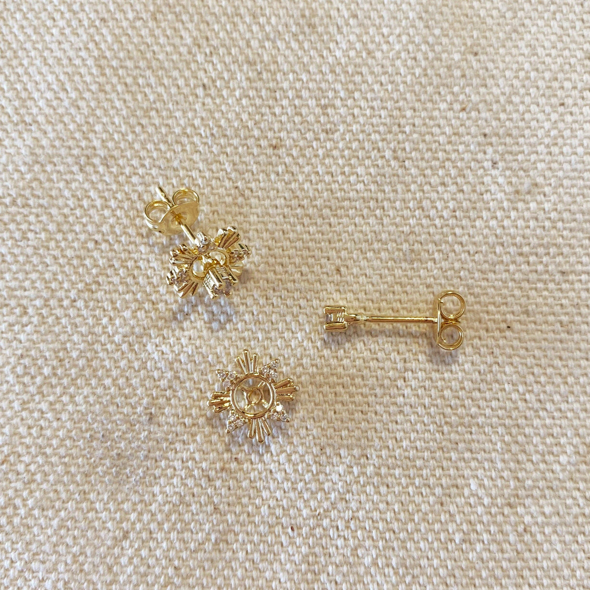 Gold earrings on a beige fabric background