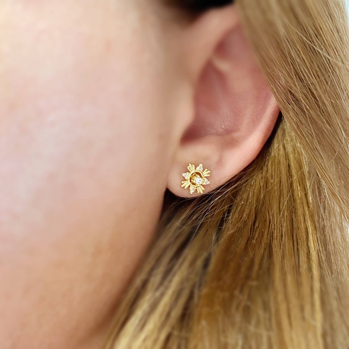 Close-up of a person wearing a gold sun-shaped earring.