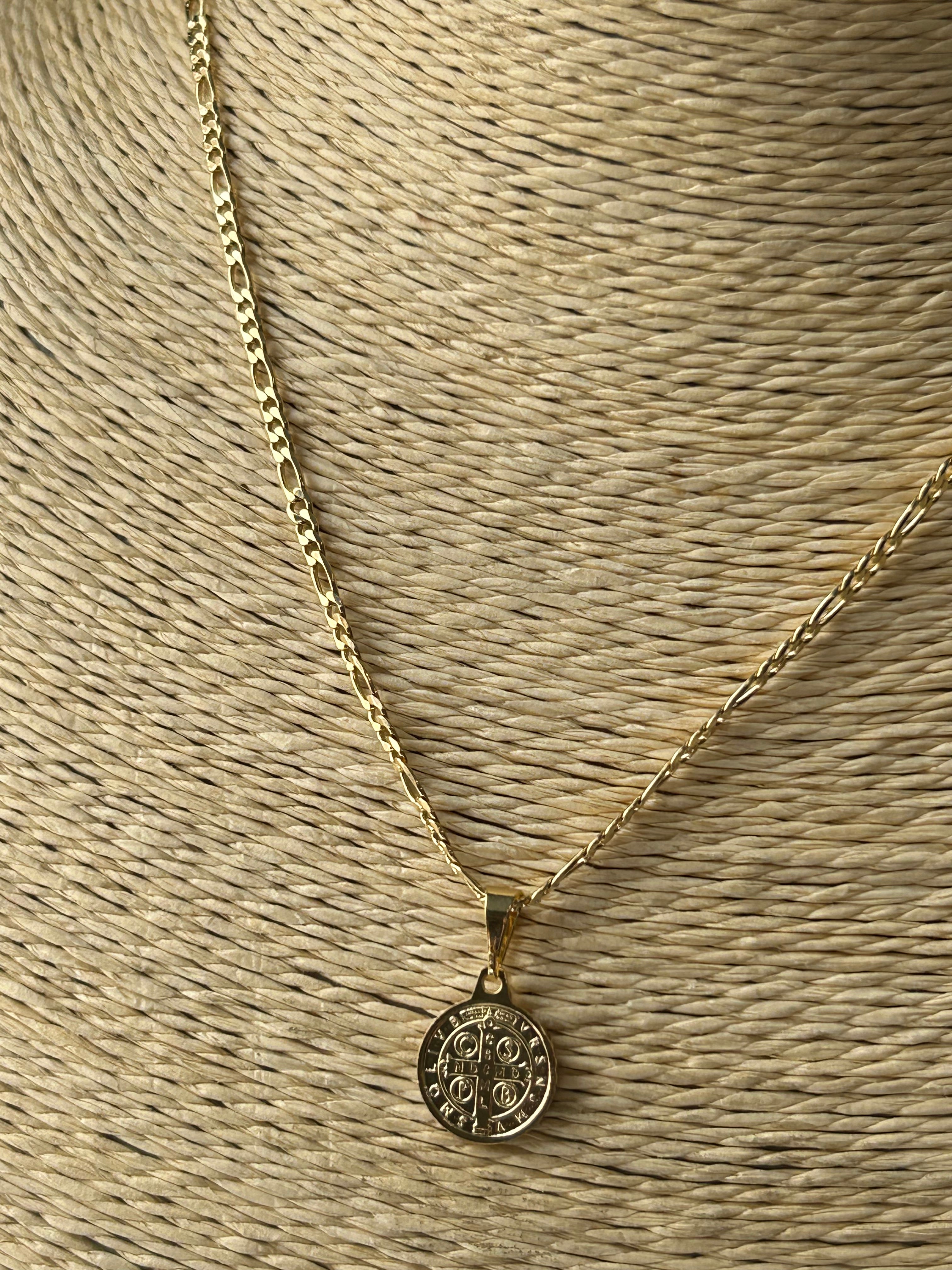 Gold necklace with a circular pendant on a textured beige surface