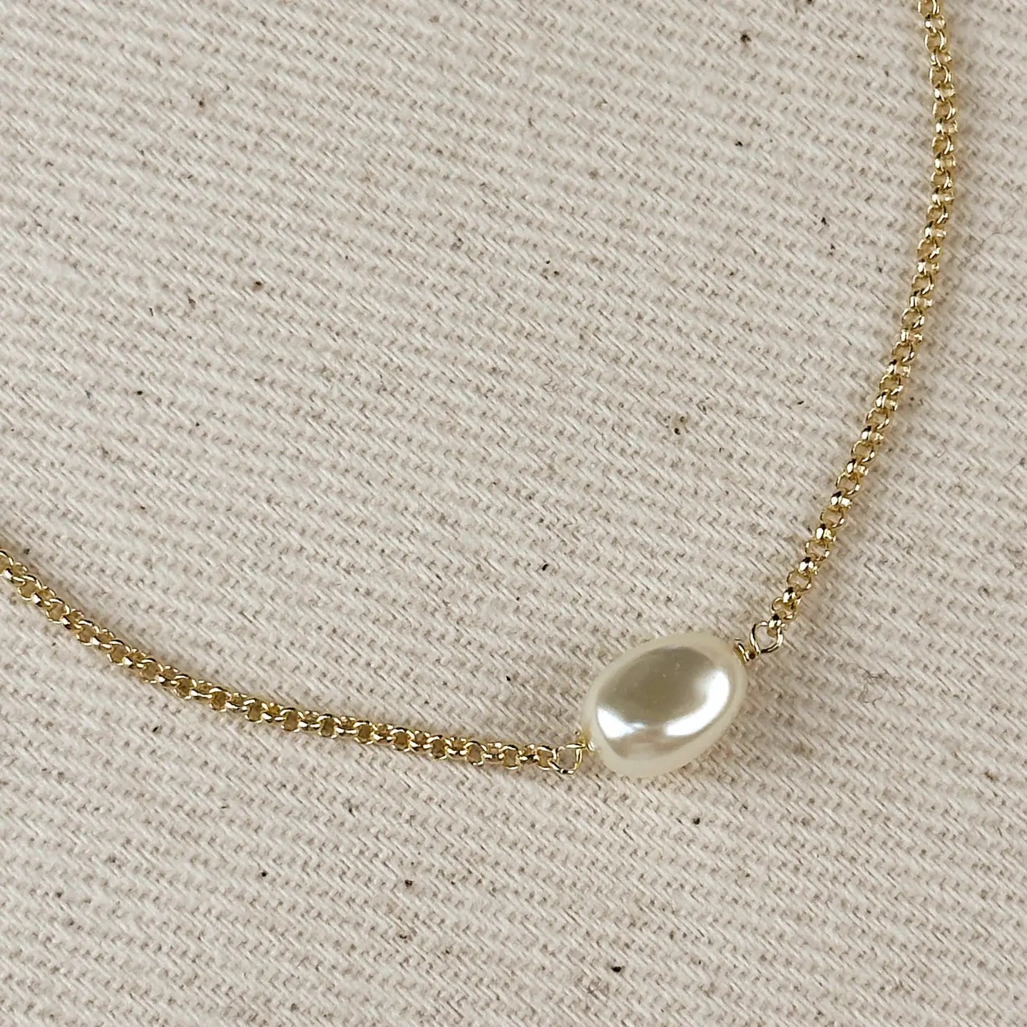 Gold necklace with a single pearl on a beige fabric background