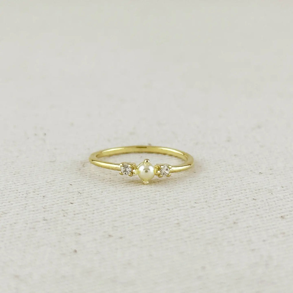 Gold ring with a pearl and small diamonds on a light beige fabric background