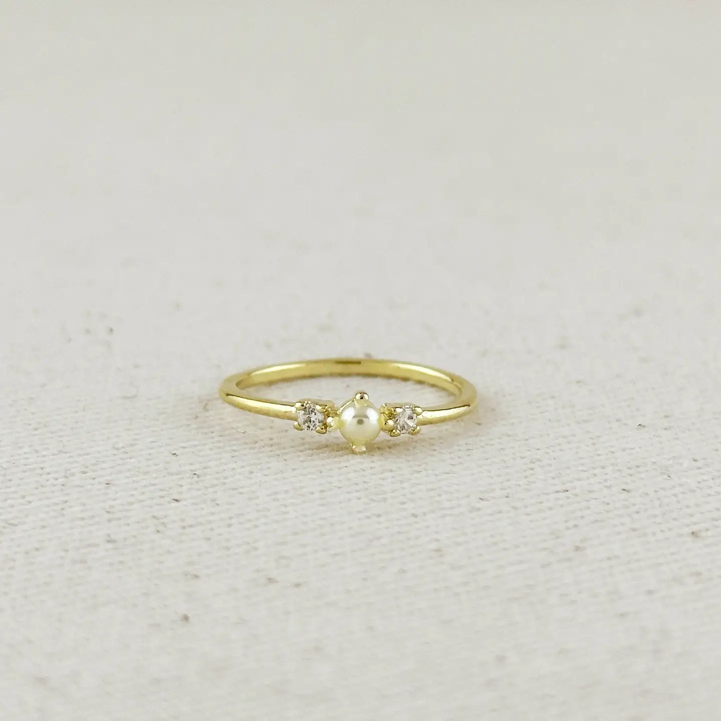Gold ring with a pearl and small diamonds on a light beige fabric background