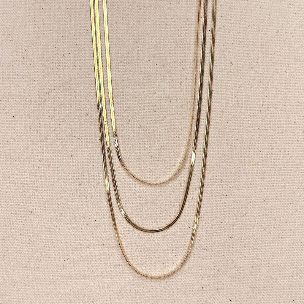 Three gold necklaces of different thicknesses on a beige fabric background