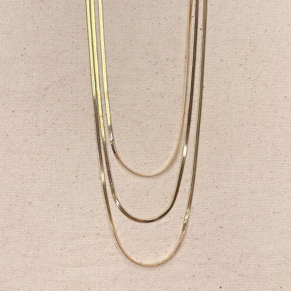 Three gold necklaces of different thicknesses on a beige fabric background