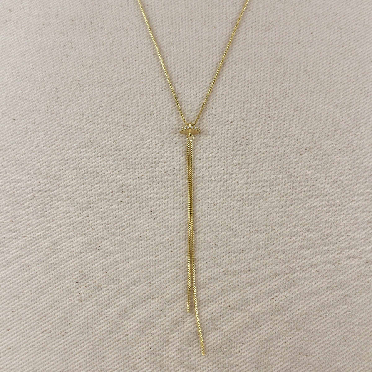 Gold necklace with a tassel on a beige fabric background