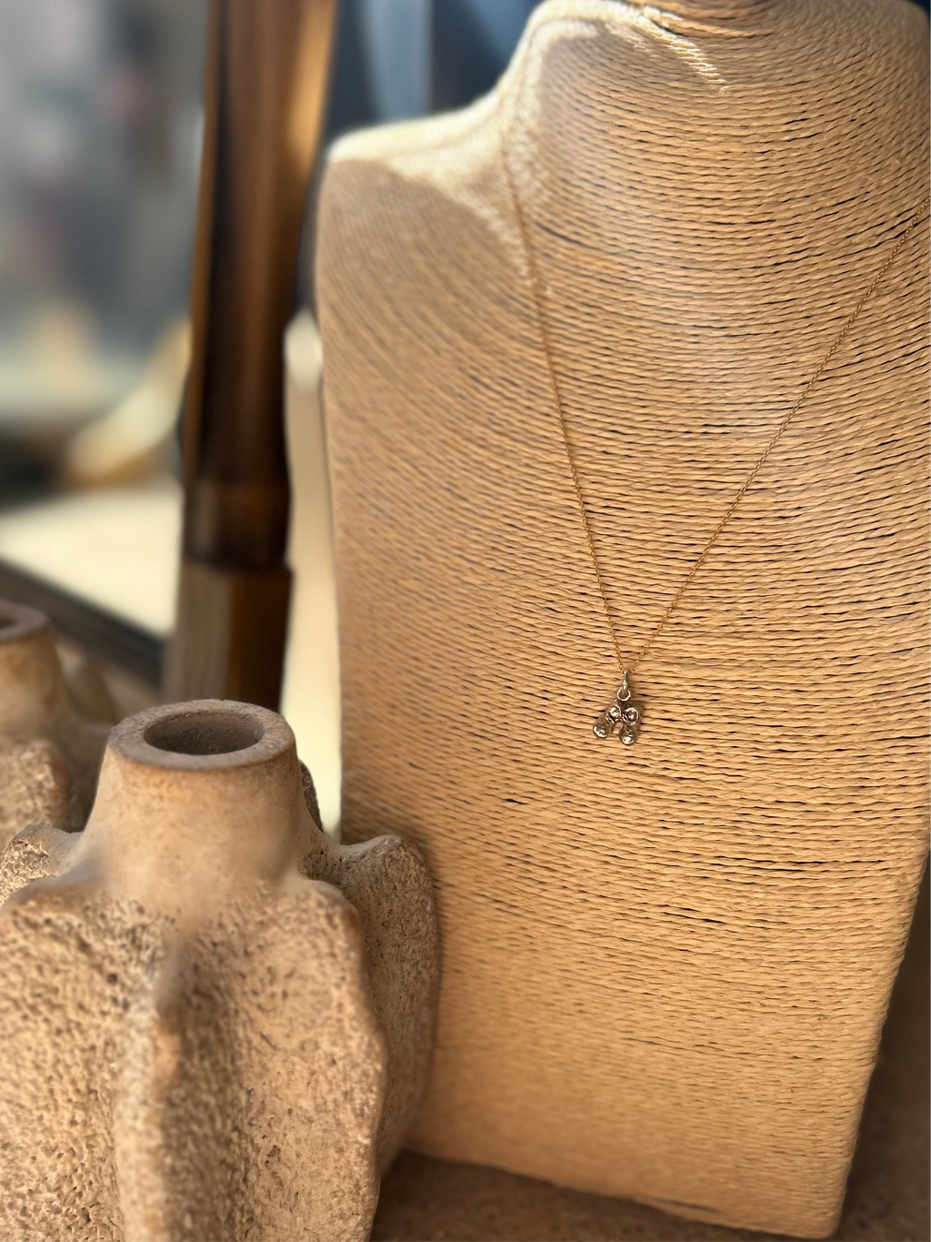 Necklace with a pendant on a textured surface next to a ceramic vase.