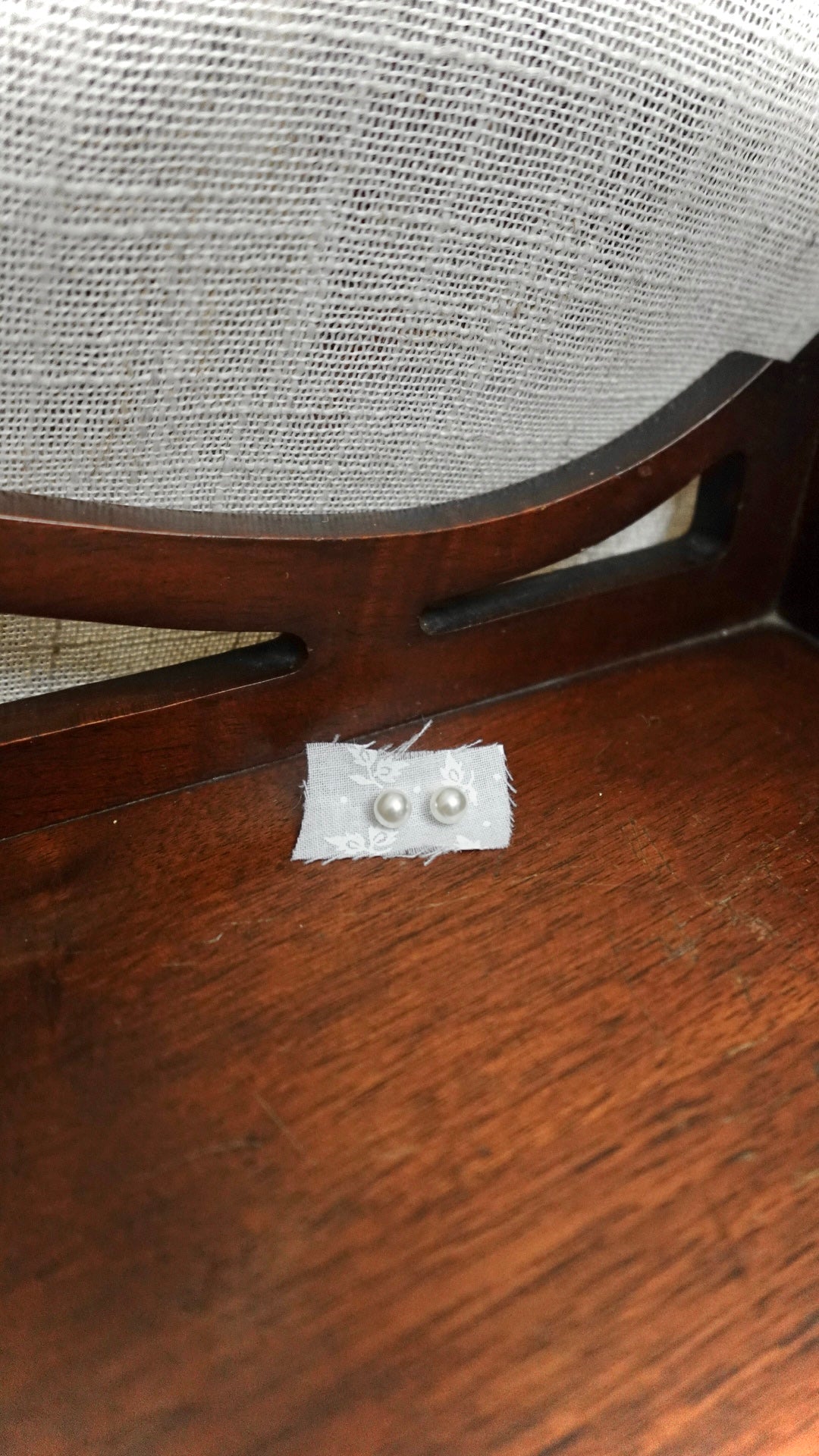 Two pearl earrings on a piece of paper with a wooden surface and fabric background