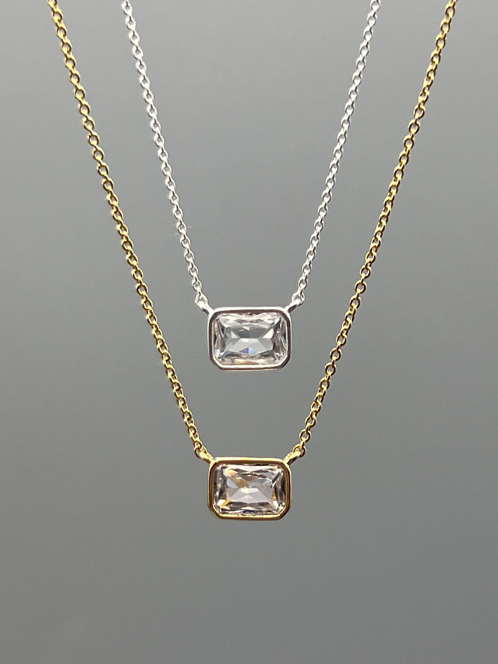Two gold necklaces with clear gemstones on a gray background