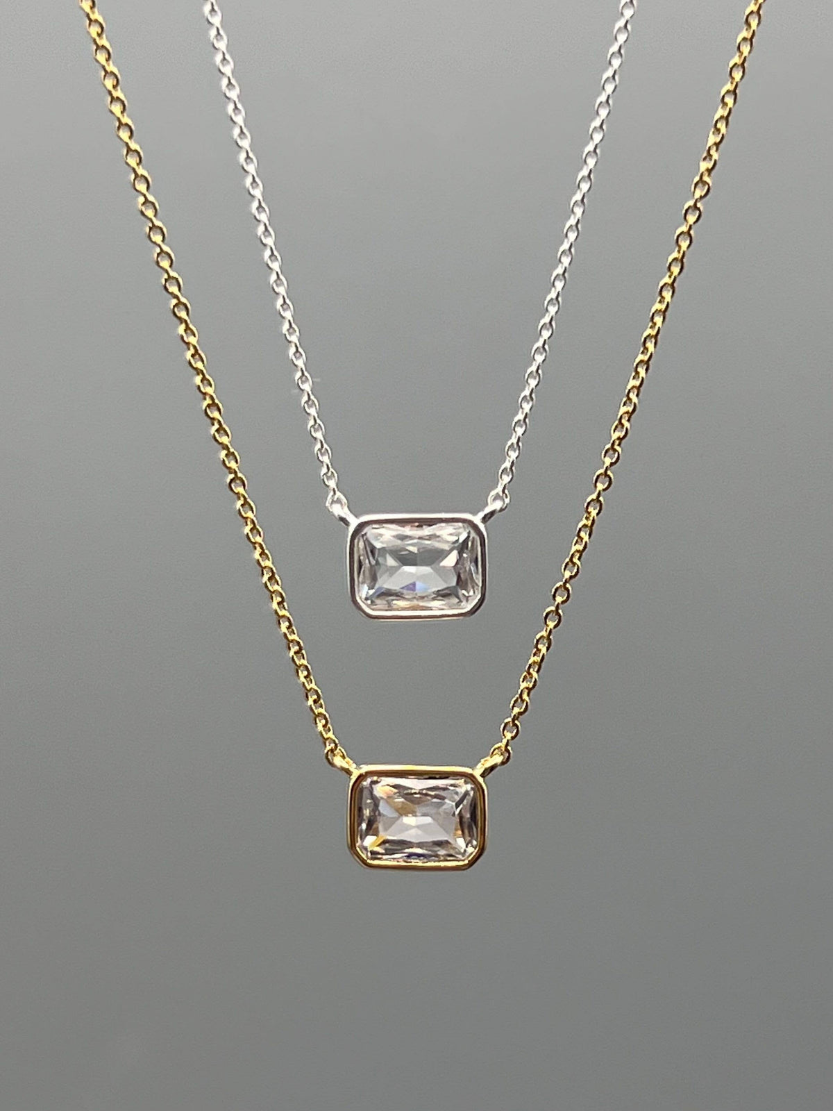 Two gold necklaces with clear gemstones on a gray background