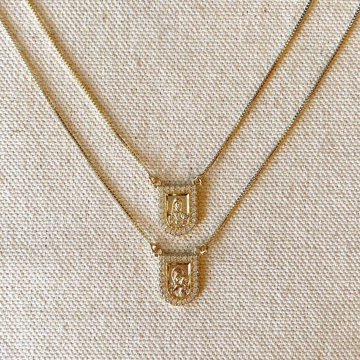 Two gold-tone necklaces with rectangular pendant charms set with clear stones, displayed against a solid white background.