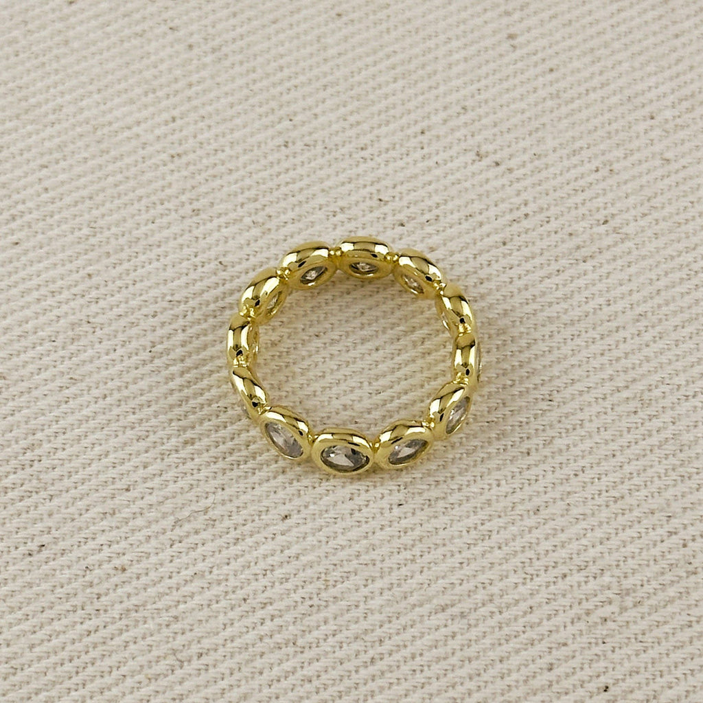 A gold band ring with small oval clear stones set along the band, photographed on a textured beige fabric background.