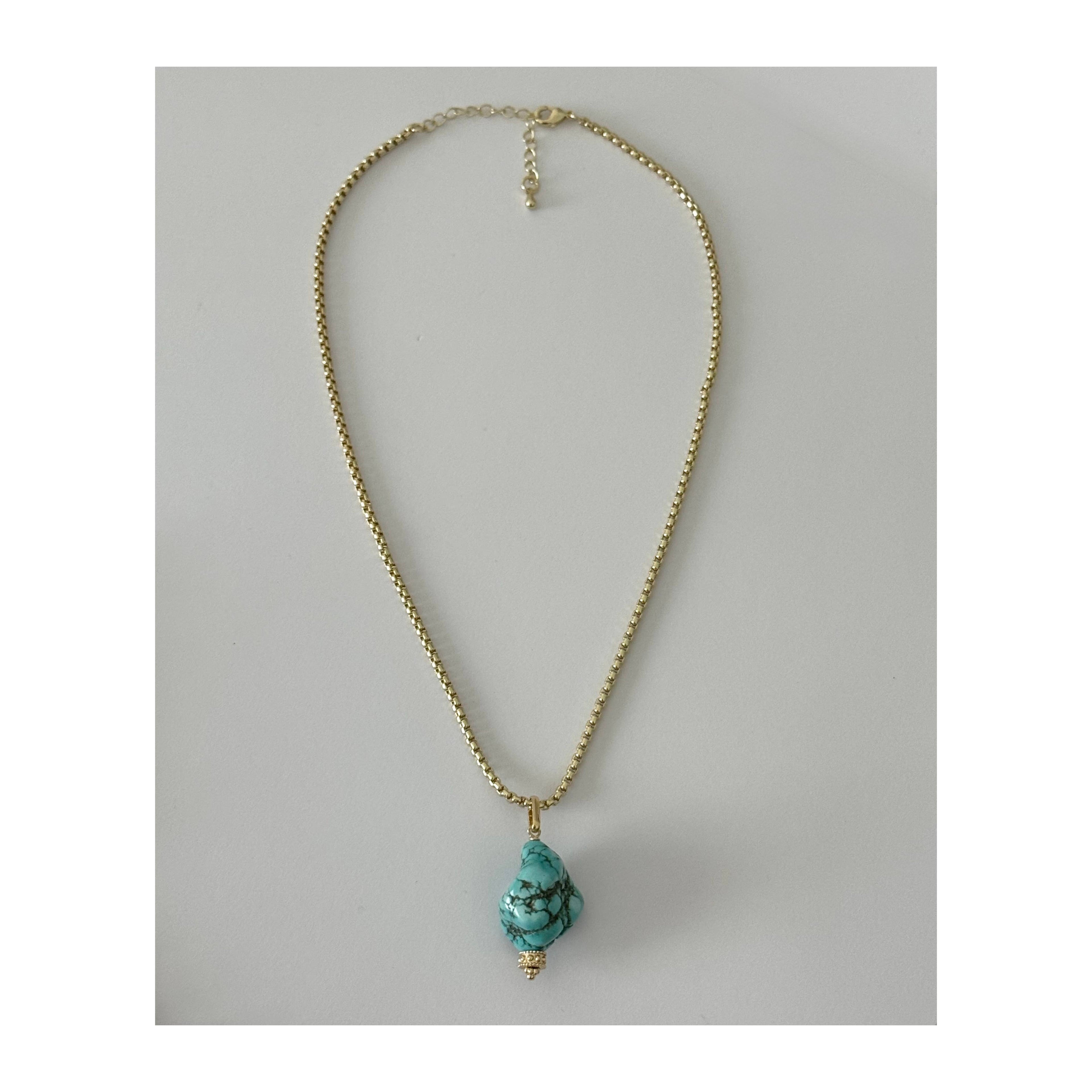 A gold chain necklace featuring a teardrop-shaped turquoise stone pendant with gold caps, displayed against a neutral gray background.