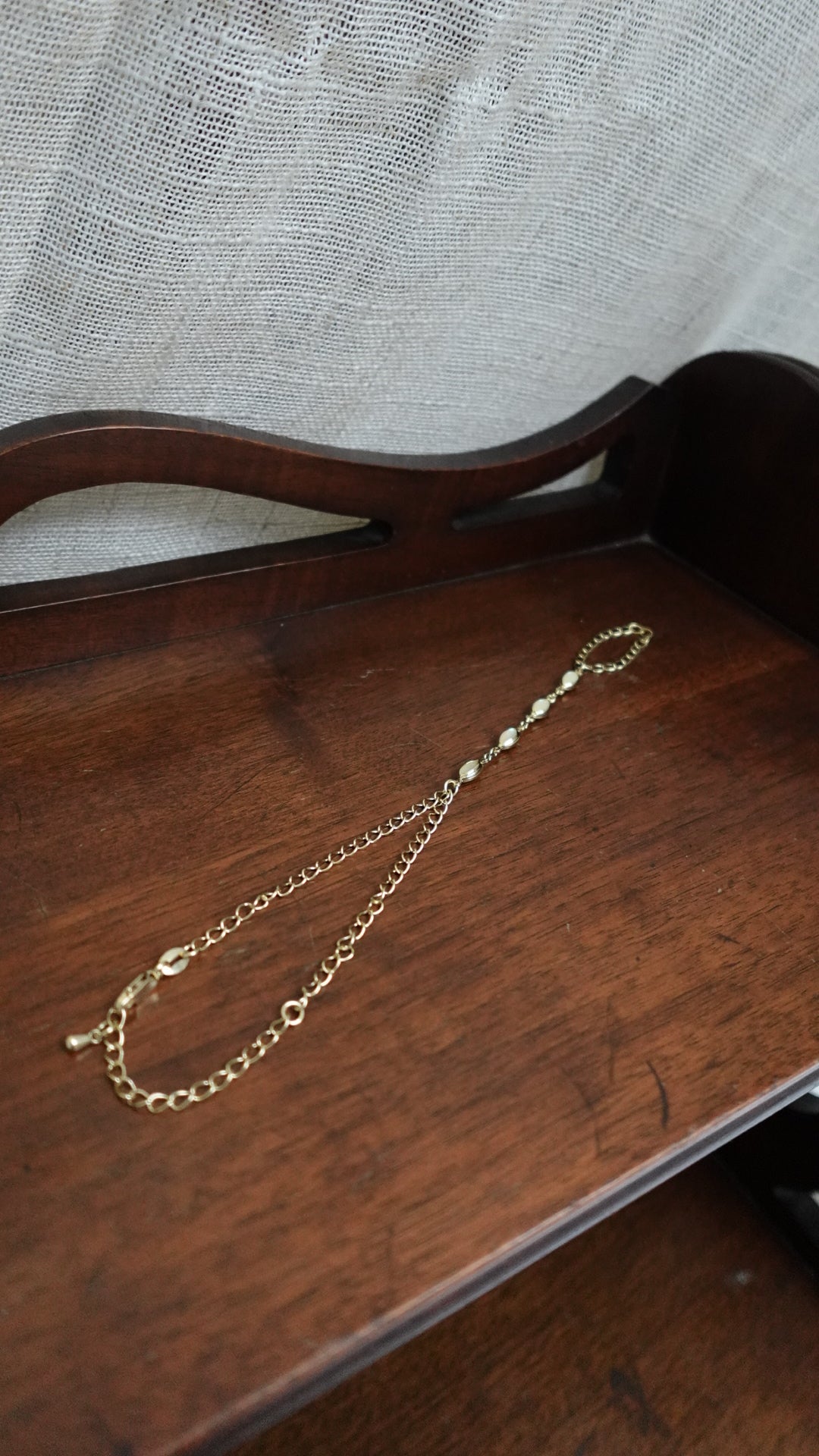 Gold necklace on a wooden surface with a textured fabric background