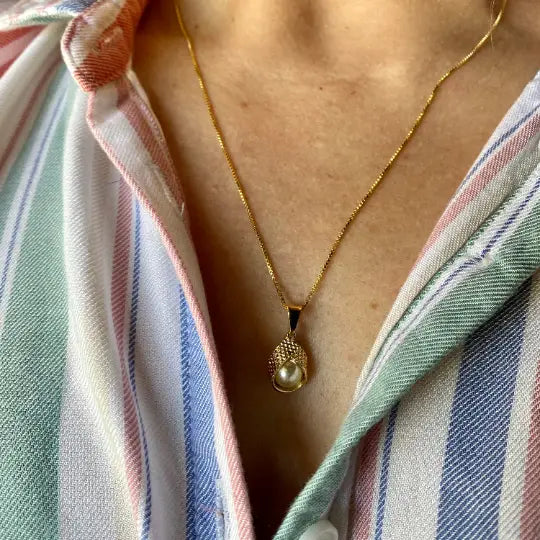 Gold necklace with a pearl pendant worn by a person in a striped shirt.