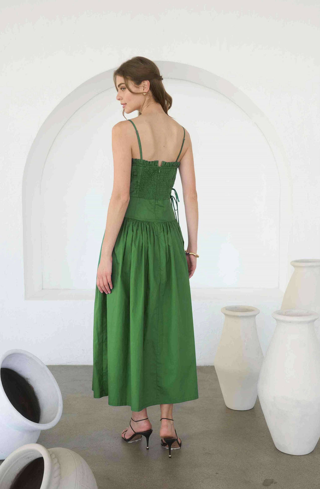 Woman wearing a green dress standing in a minimalistic room with white arch and vases.