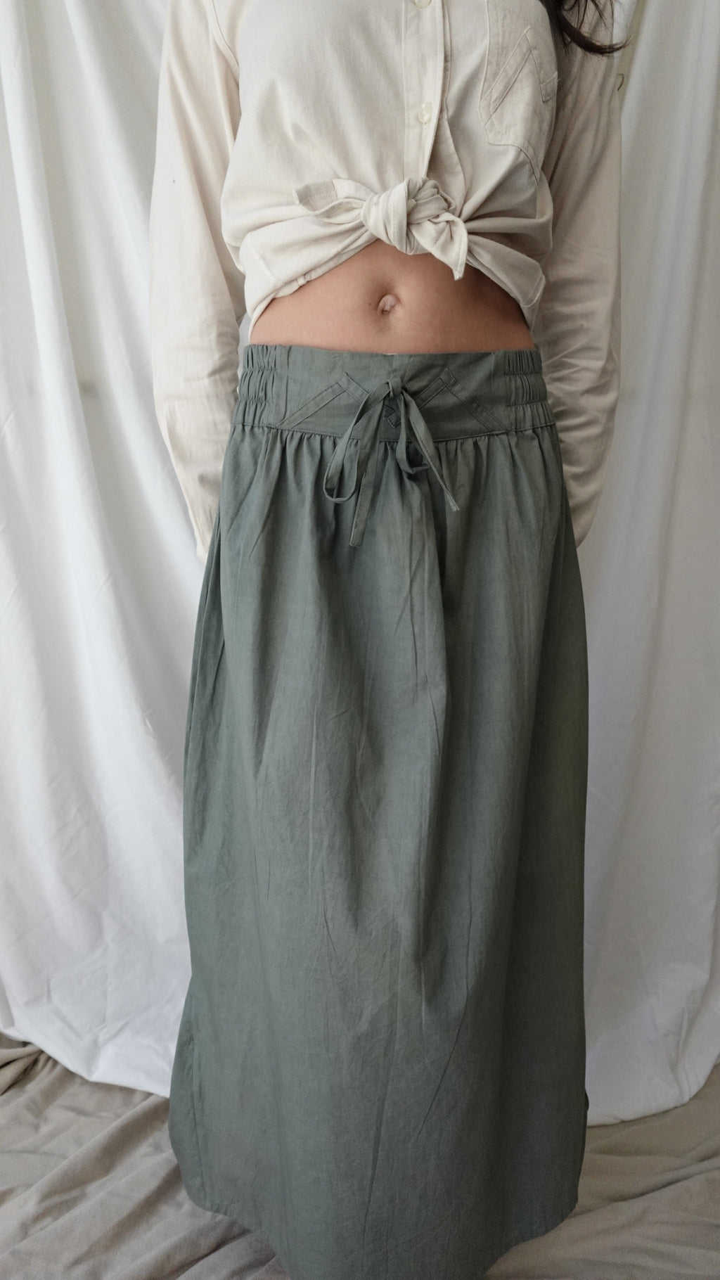 Person wearing green pants and a beige top on a white bed.